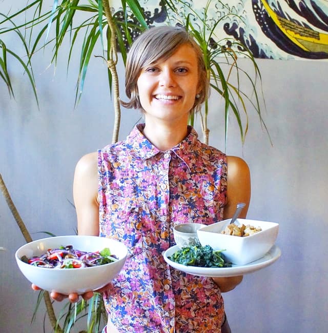 Portrait of Caylee Clay. Caylee is smiling and holding plates of colorful foods.